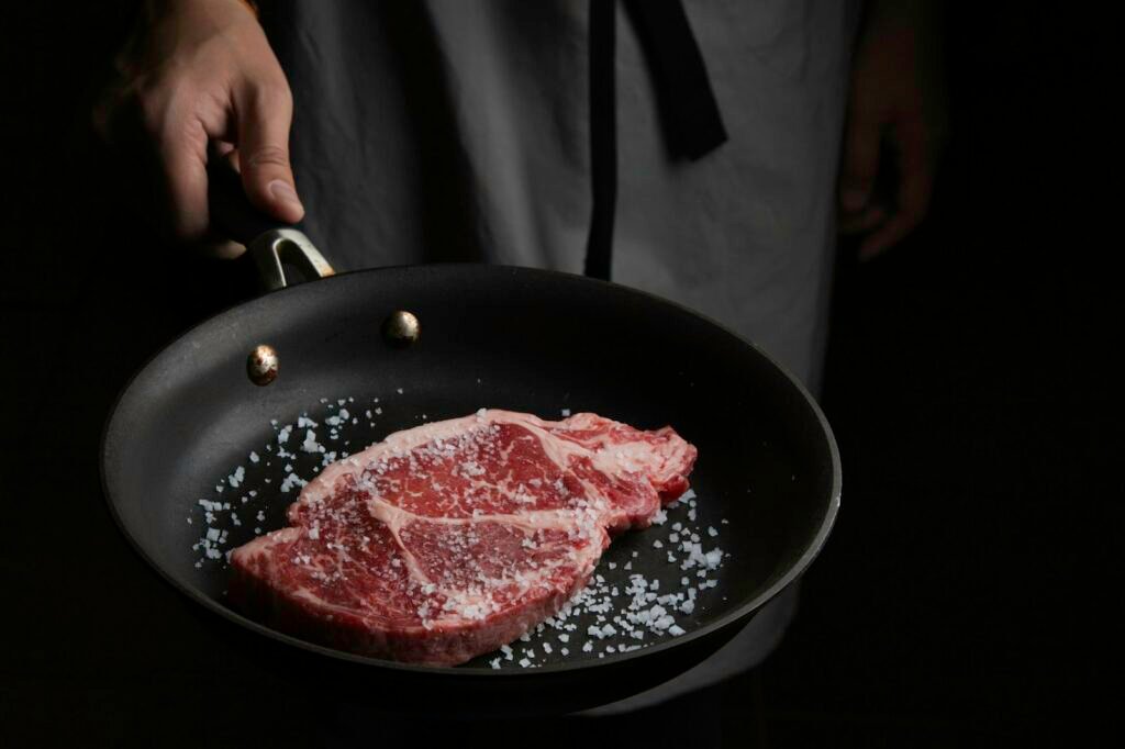 how to cook rib eye steak in a hot pan: raw rib eye salted in a heavy pan